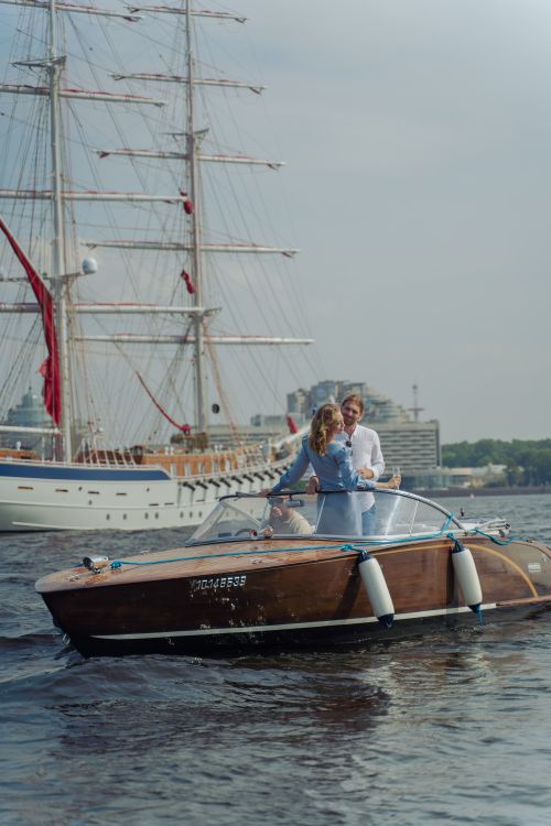 Free Couple enjoying a romantic boat ride in Saint Petersburg with a scenic backdrop featuring elegant ships. Stock Photo