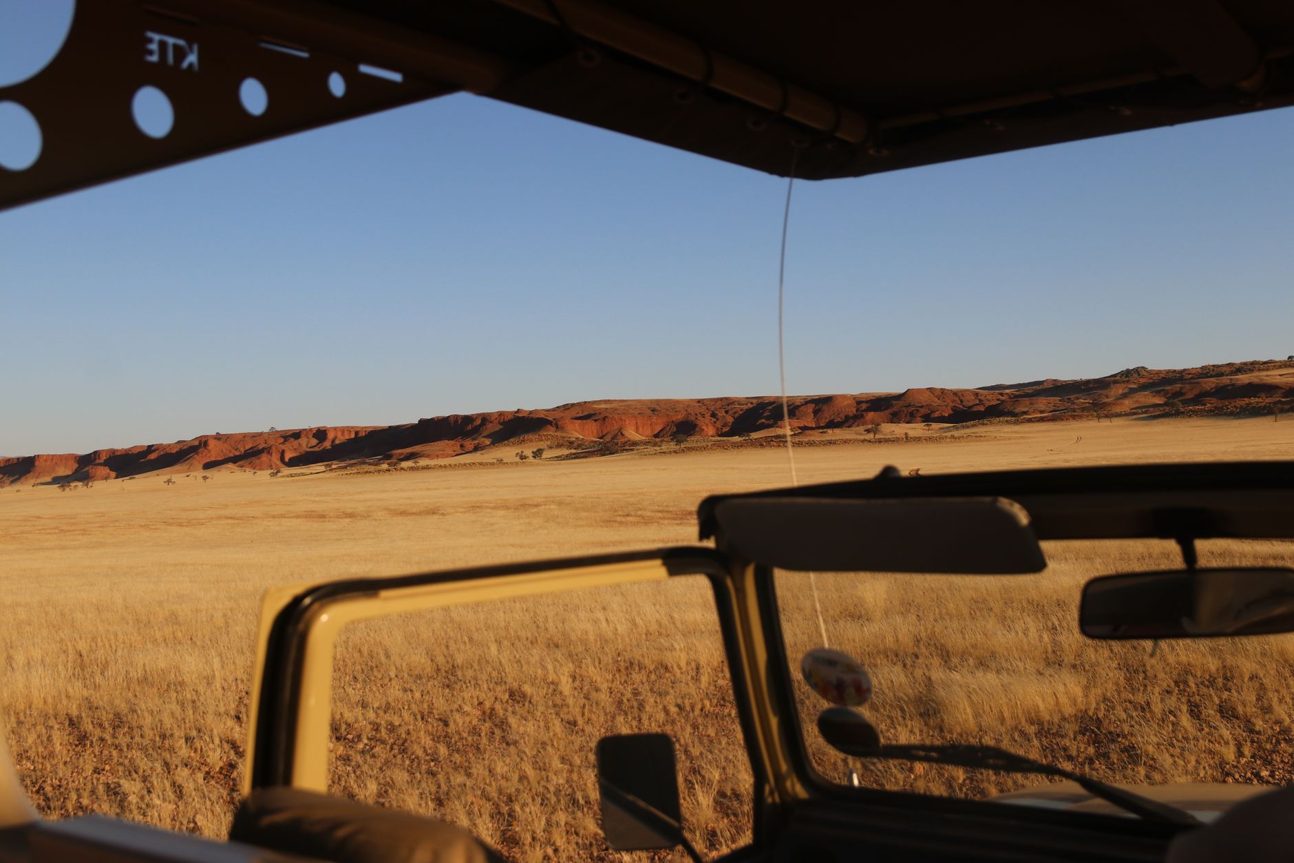 Capture of Namibian desert landscape from a jeep, showcasing rugged red rock formations.