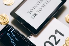 Tablet with investment question amidst bitcoins and 2021 planner. Analyze crypto trends.