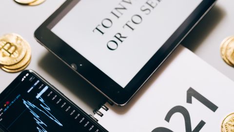 Tablet with investment question amidst bitcoins and 2021 planner. Analyze crypto trends.
