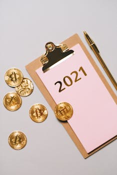 Gold bitcoin coins with a clipboard and pen on a white surface, symbolizing cryptocurrency trends.