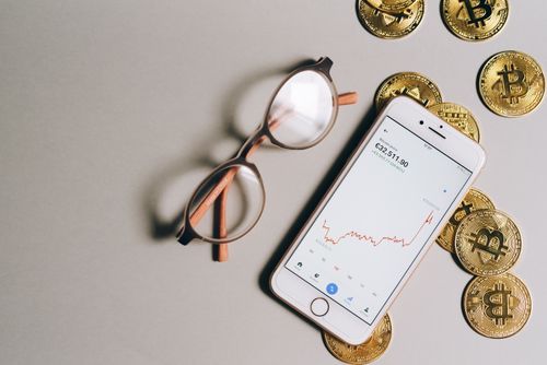 Free Flat lay of Bitcoin coins, eyeglasses, and smartphone displaying cryptocurrency graph. Stock Photo