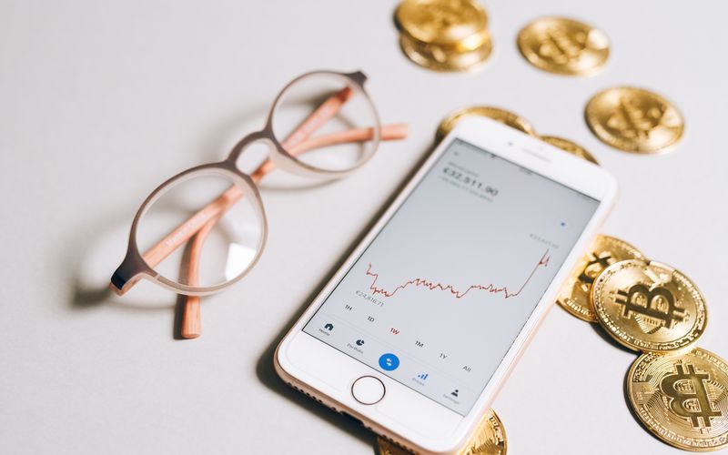 Smartphone displaying a cryptocurrency graph alongside bitcoin coins and eyeglasses