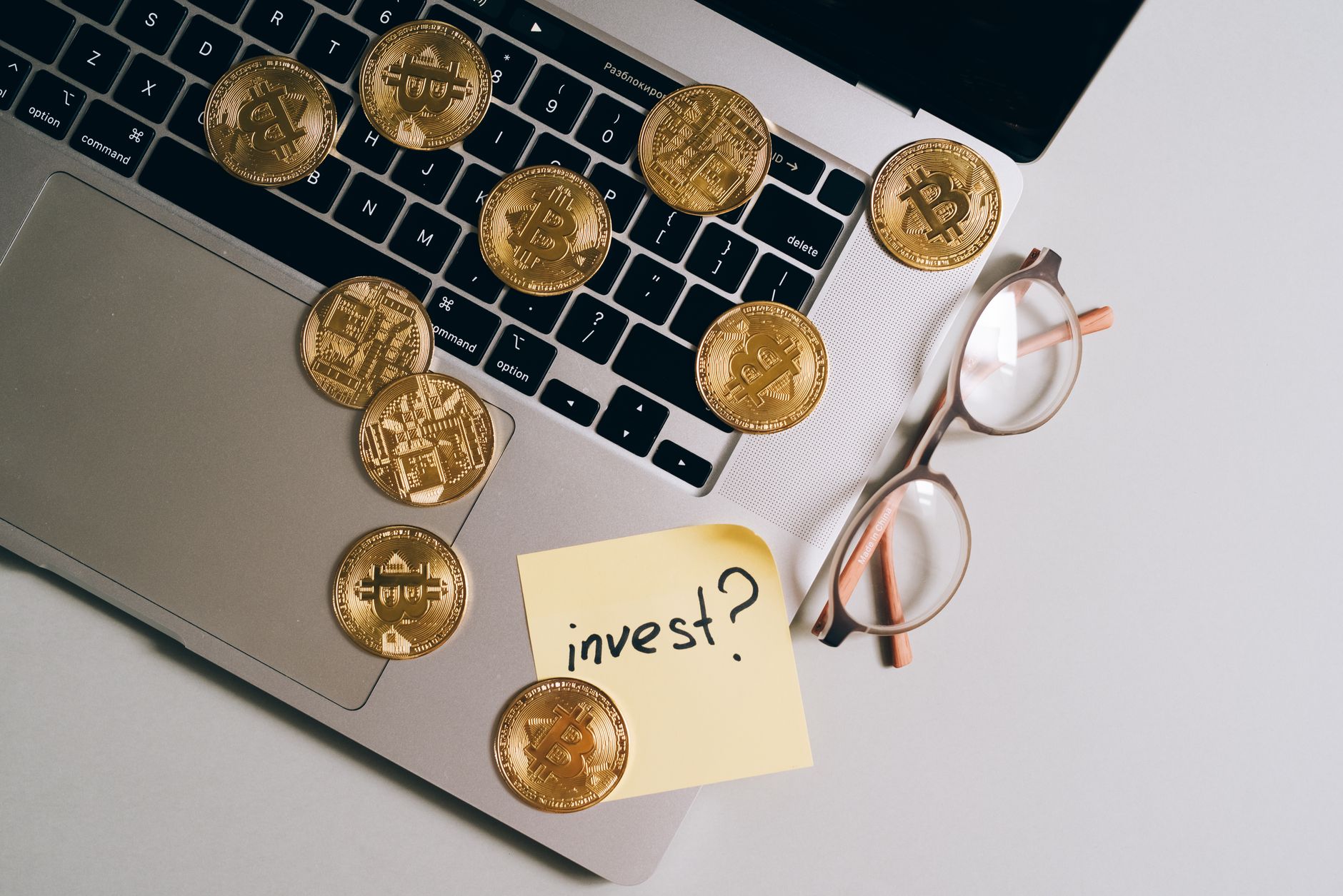 Laptop with Bitcoin coins, eyeglasses, and 'invest?' note. Ideal for finance and tech themes.