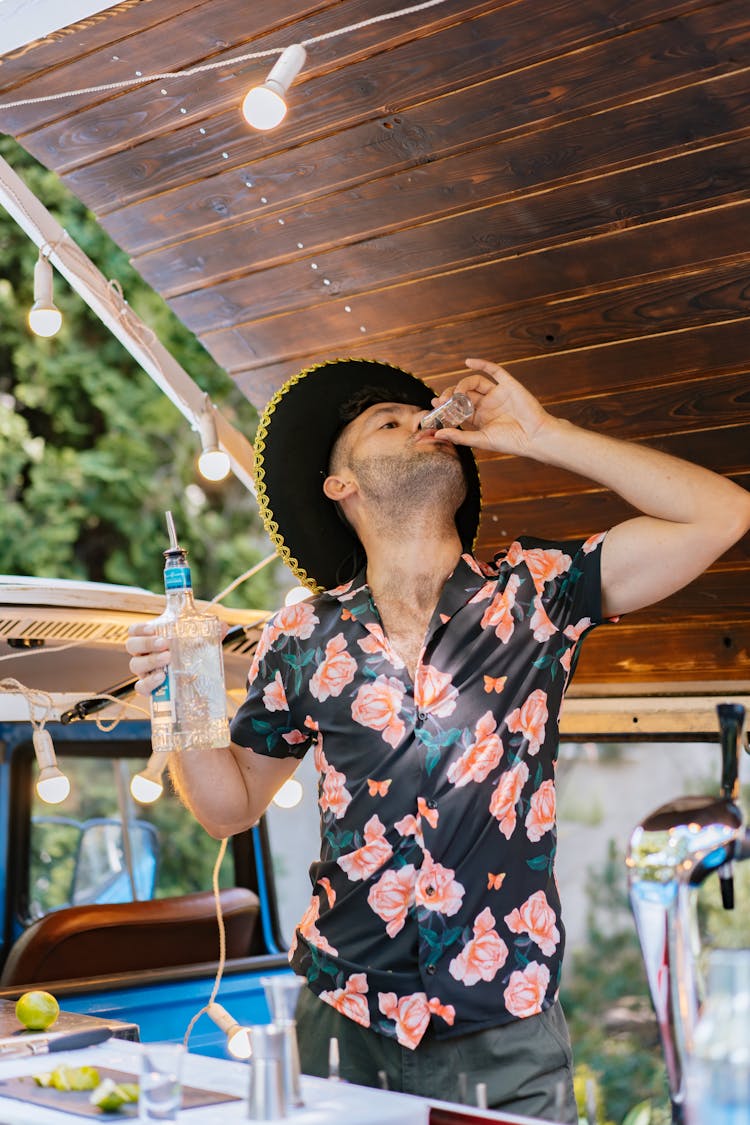 A Man In A Black Floral Shirt And Sombrero Drinking A Shot Of Tequila