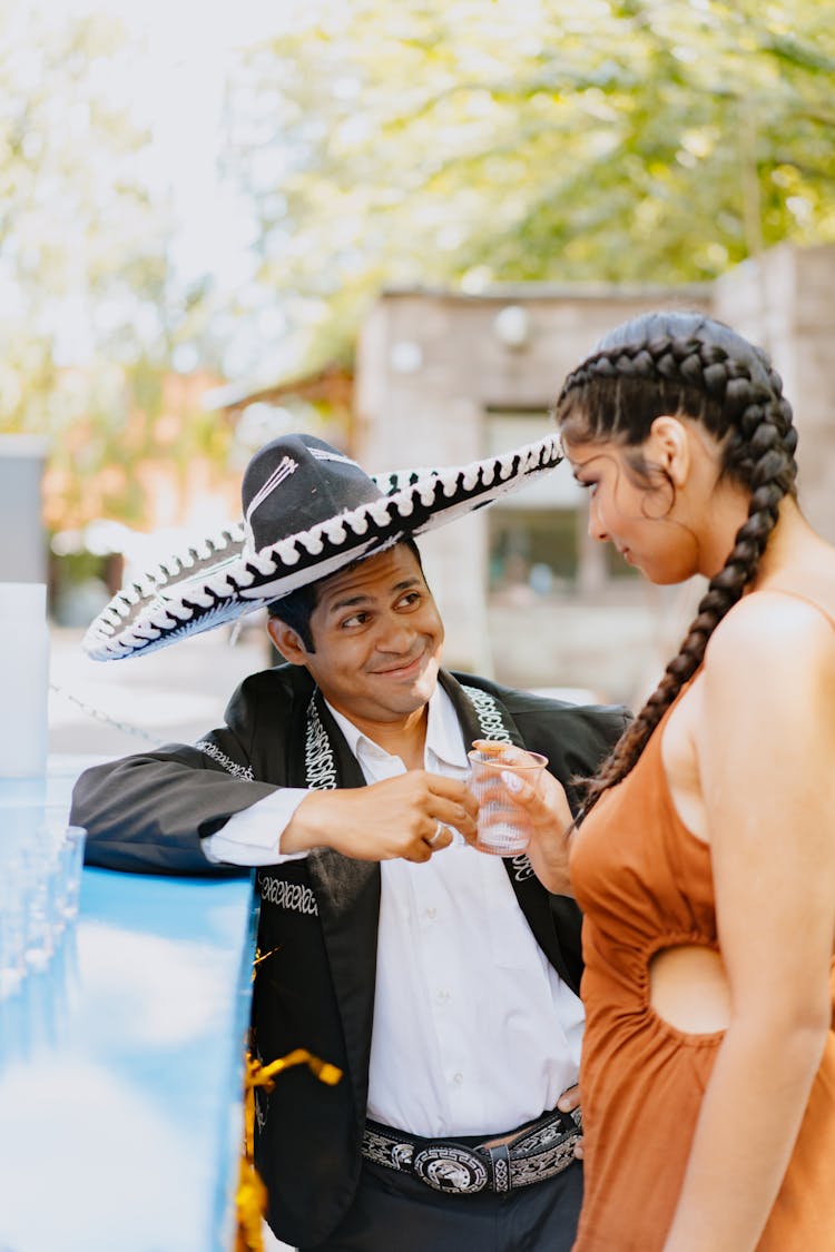 Man In Traditional Clothing Standing With A Woman Having A Drink 