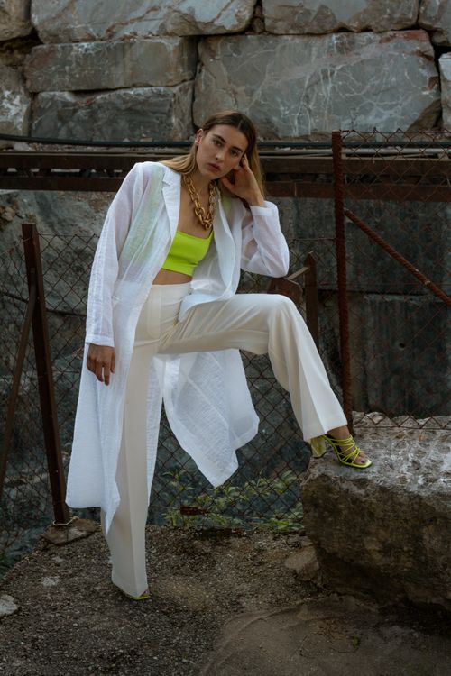 Free Stylish woman posing in white attire and green crop top against urban backdrop. Stock Photo