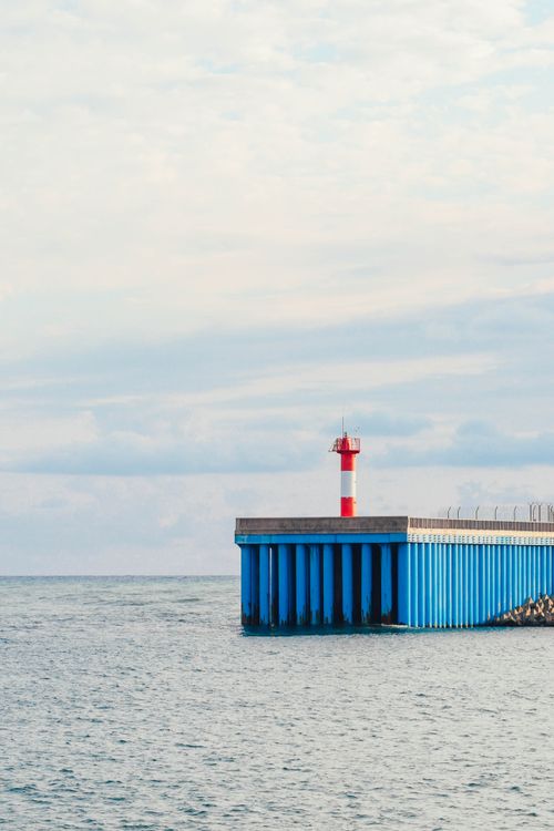 Free Serene view of a lighthouse on a pier overlooking the tranquil sea in Adler, Russia. Stock Photo