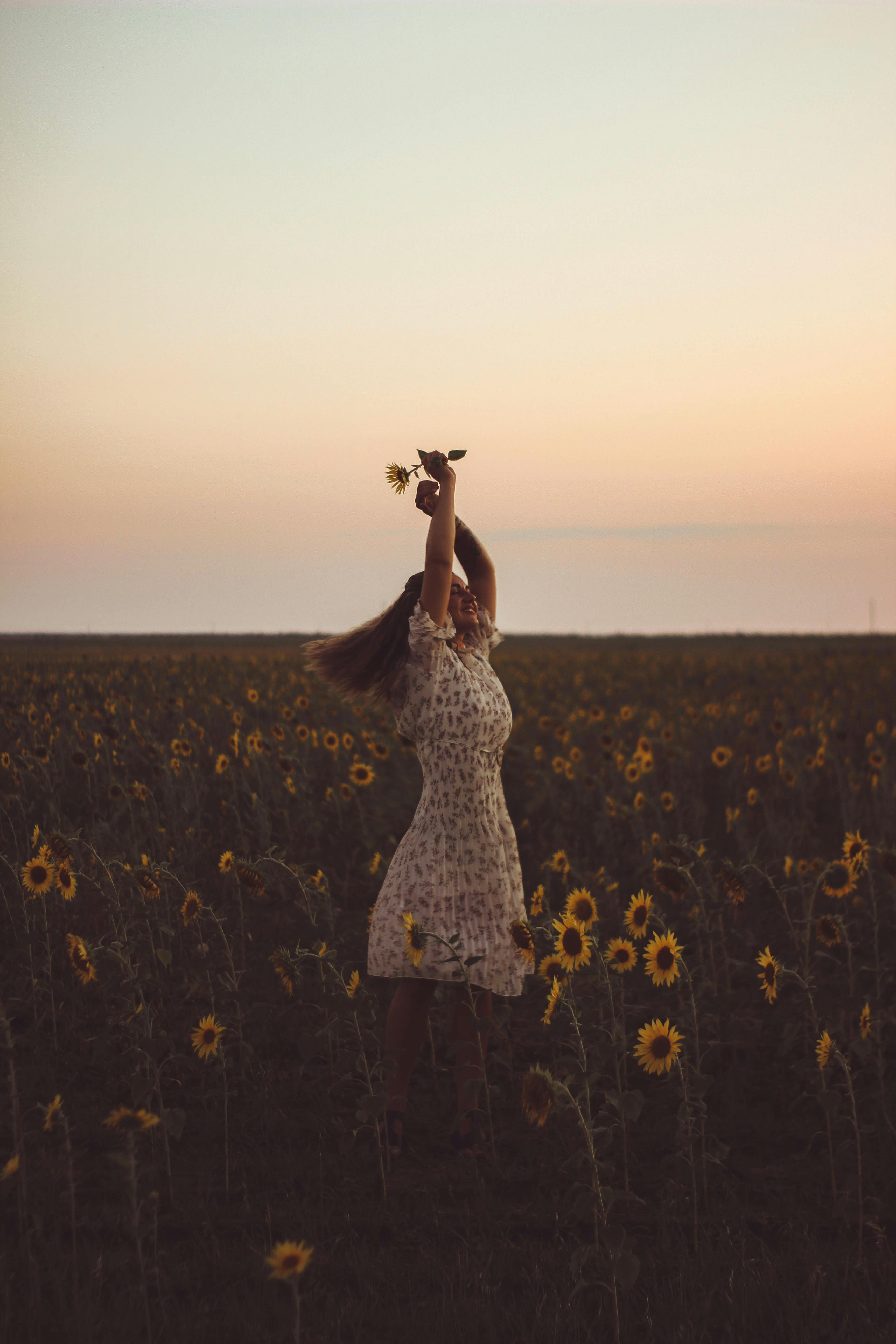 Woman enjoying the beauty of a sunflower field at sunset, embracing nature's tranquility.