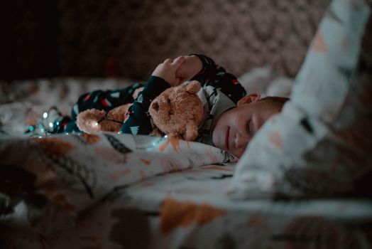 A young child peacefully sleeping in bed, hugging a teddy bear close, creating a cozy bedtime atmosphere.