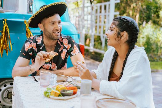 Friends enjoying a lively meal outdoors with vibrant hats and casual attire, filled with laughter.