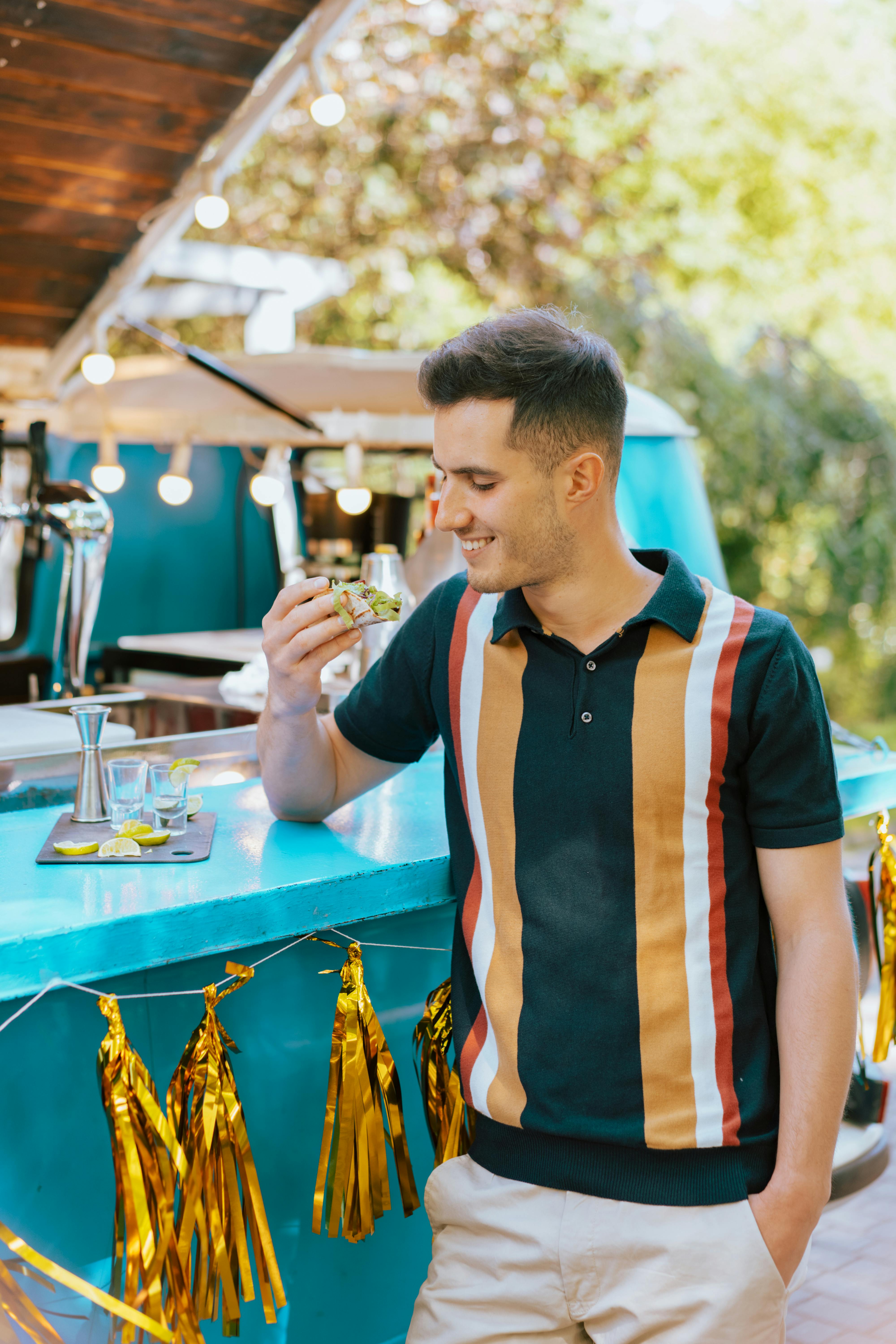 Free Smiling man holding a drink at a festive outdoor bar setup during daytime. Stock Photo
