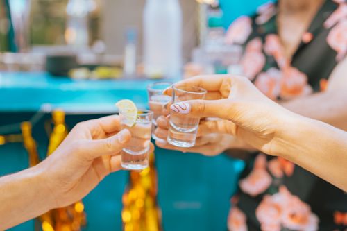Free Close-up of people toasting with tequila shots in a festive outdoor setting. Stock Photo