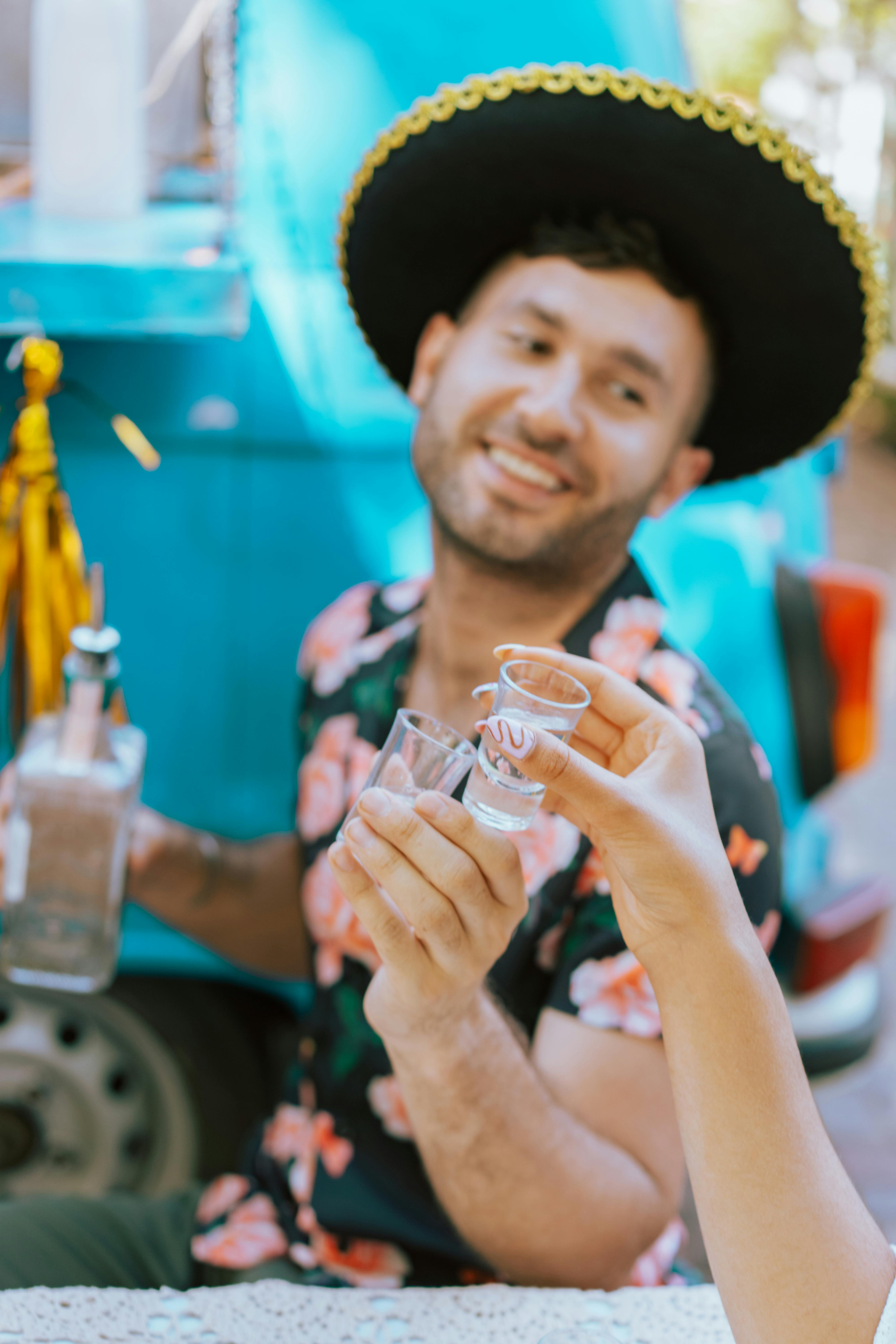 Free A man in a sombrero celebrates outdoors with tequila and friends on a sunny day. Stock Photo