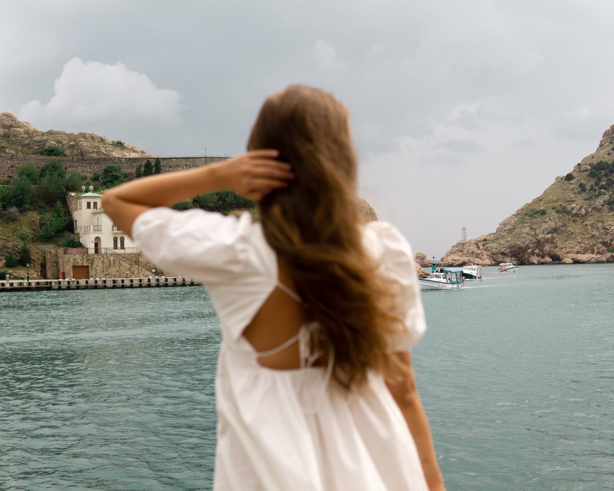 A woman in a white dress near the water — the linen summer dress, the hero of a European summer wardrobe