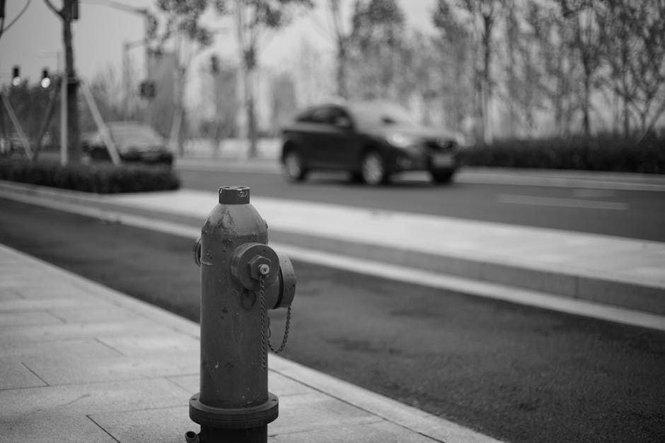 Monochrome image of a fire hydrant with a blurred background of a city street and passing car.