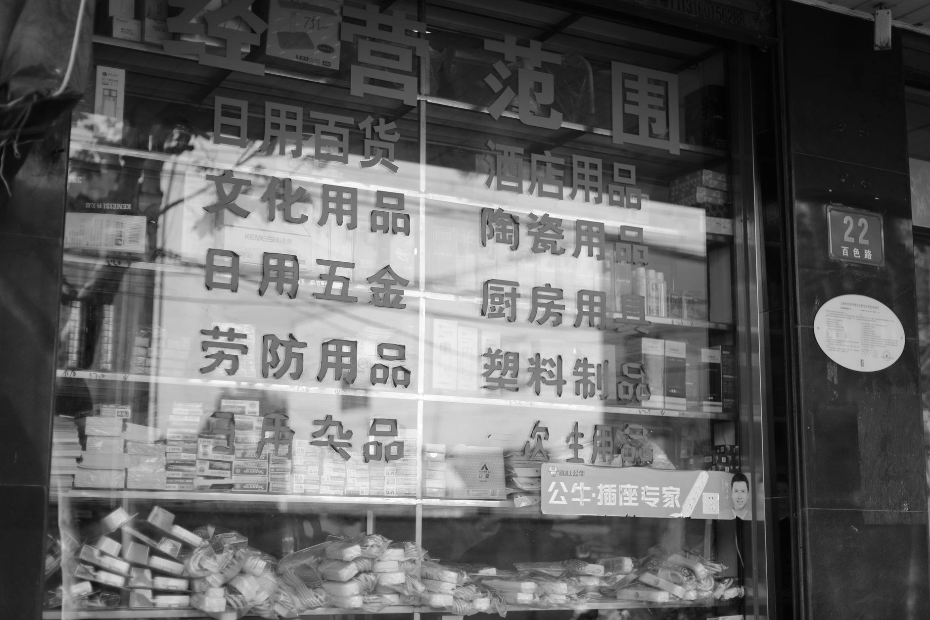 Black and white photo of a Chinese store window display showing various products and signage.