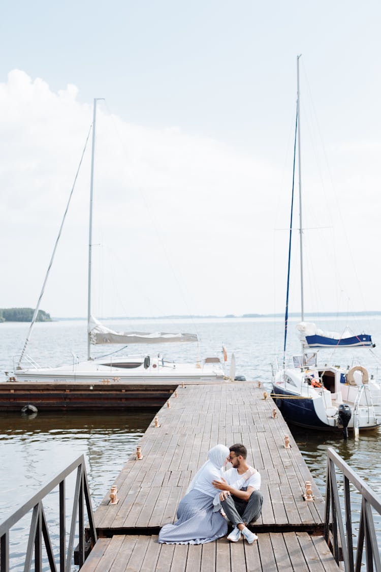 A Couple Sitting On A Wooden Dock