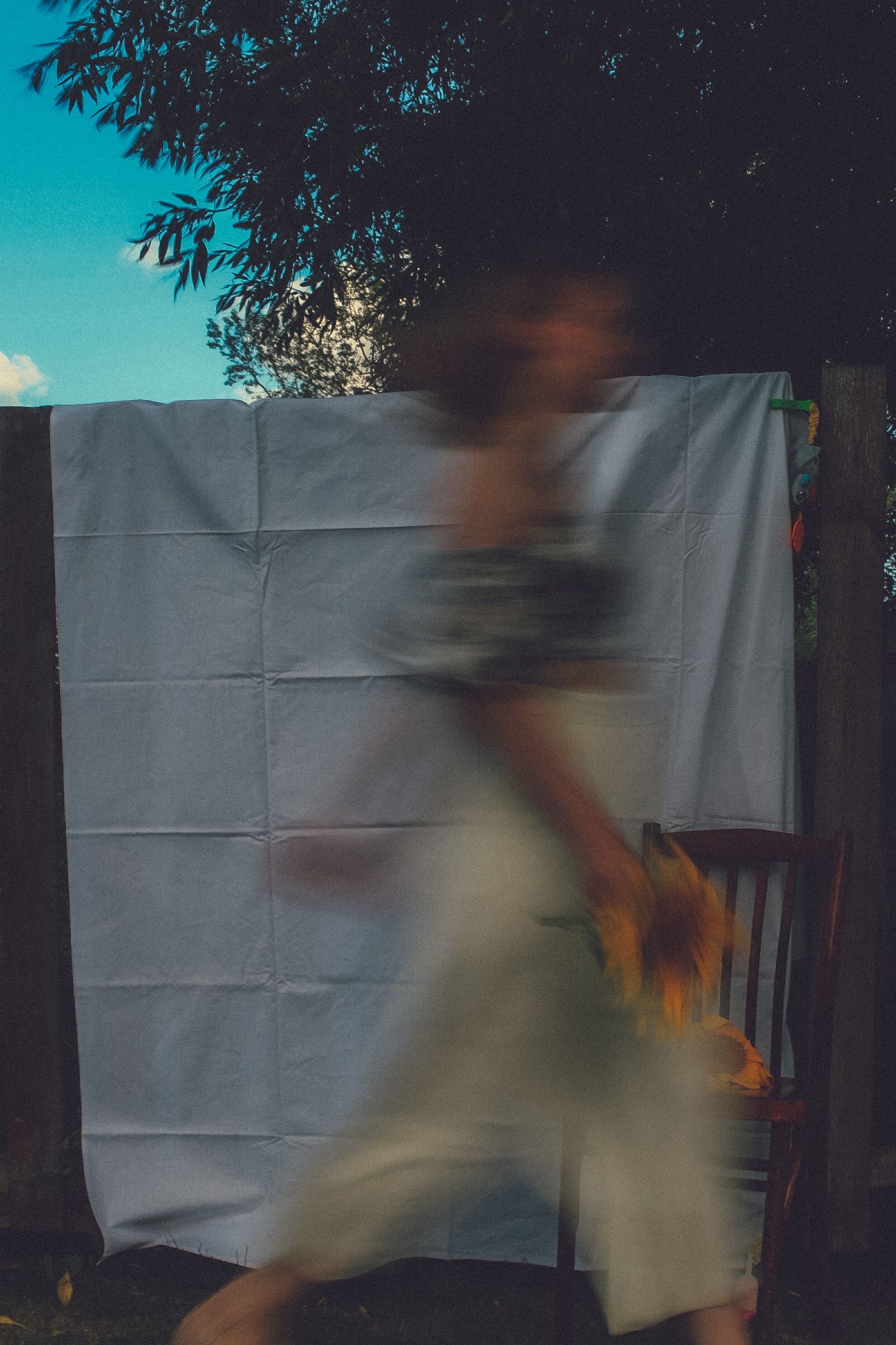 Abstract image with a blurred woman walking past a chair and fabric outdoors.