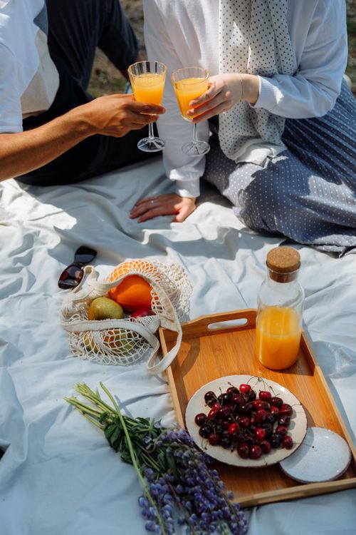 Free A delightful picnic scene with fresh fruits, juice, and cheerful toasting in a sunny setting. Stock Photo
