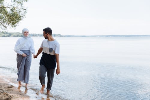 Photo of a Couple Holding Hands while Walking at the Beach