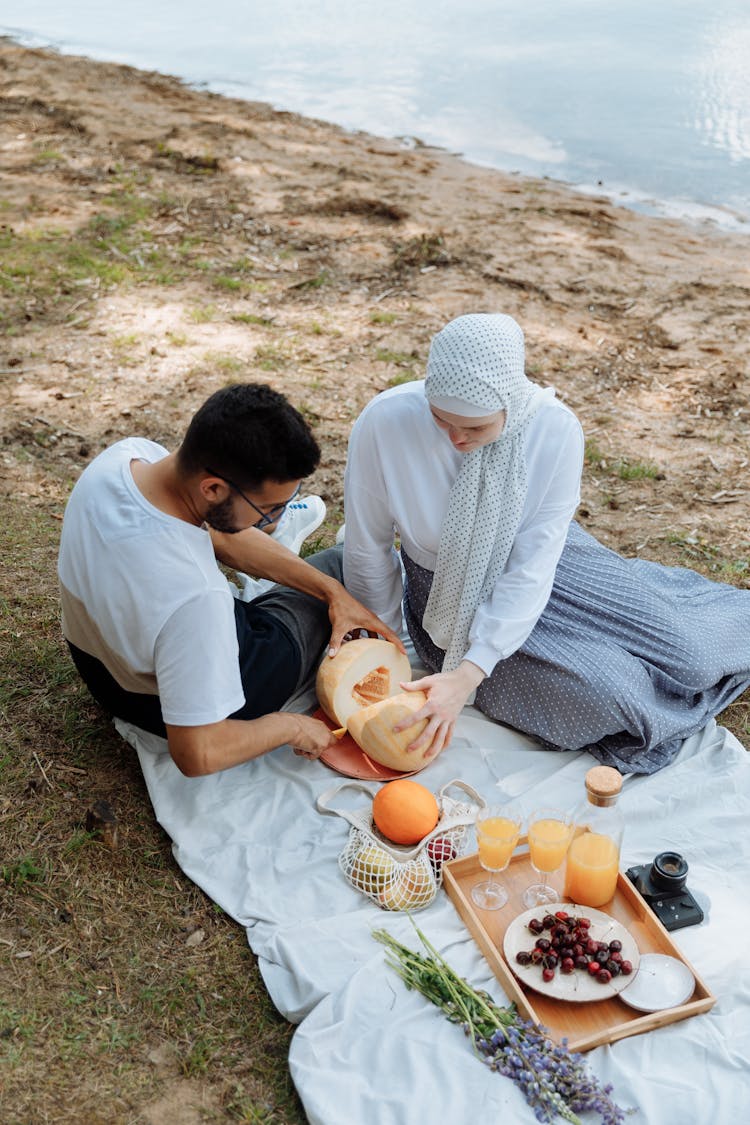 A Couple Slicing A Fruit On The Picnic Mat