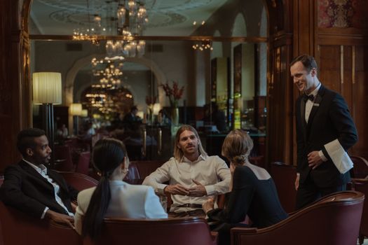 A sophisticated group enjoying a luxurious dinner with attentive waiter service in an upscale restaurant.