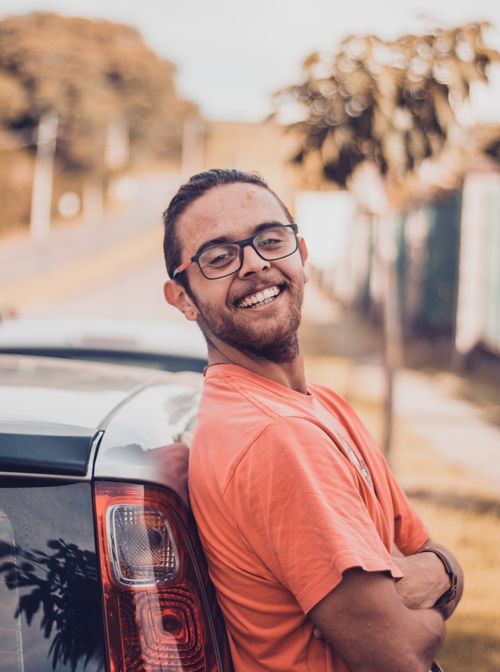 Free Happy man with eyeglasses and beard leaning on car in a sunny outdoor setting. Stock Photo