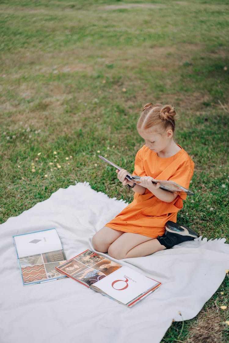 A Girl Reading Books On A Blanket Outdoors