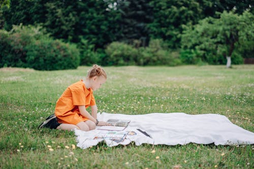 A Girl Reading Books on a Blanket Outdoors