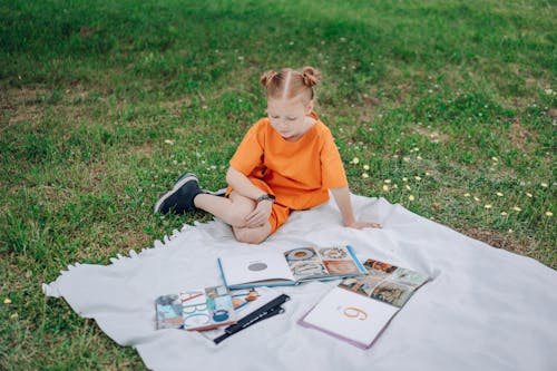 A Girl Reading Books on a Blanket Outdoors