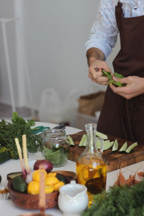 Free Man in kitchen apron preparing fresh vegetables and herbs for a healthy meal. Stock Photo