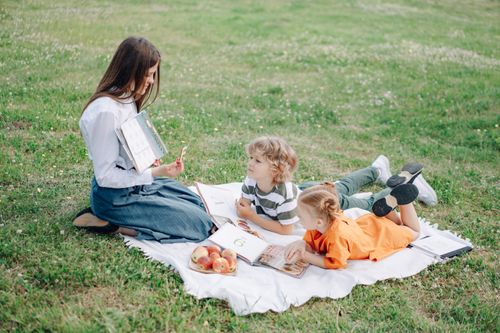 Free A young teacher conducting an outdoor learning session with children, engaging in interactive study on a grassy field. Stock Photo