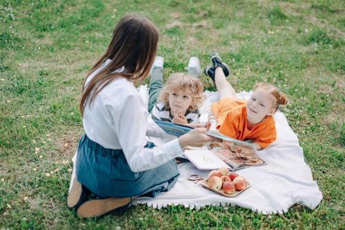 Free Children and teacher studying outdoors on a picnic mat with books and snacks. Stock Photo