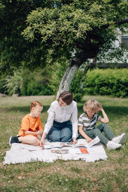 Free A woman teaches two kids outdoors on a picnic blanket under a tree. Stock Photo