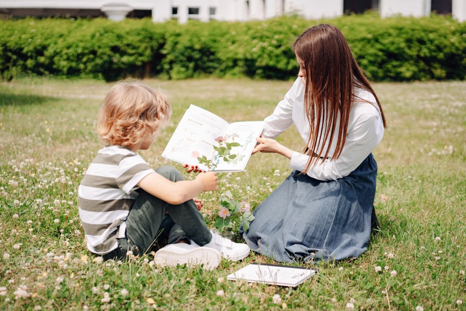 Woman teaching child about plants outdoors with a book on a sunny day.
