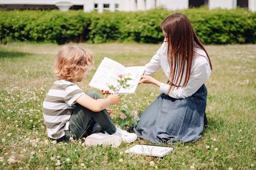 Free Woman teaching child about plants outdoors with a book on a sunny day. Stock Photo