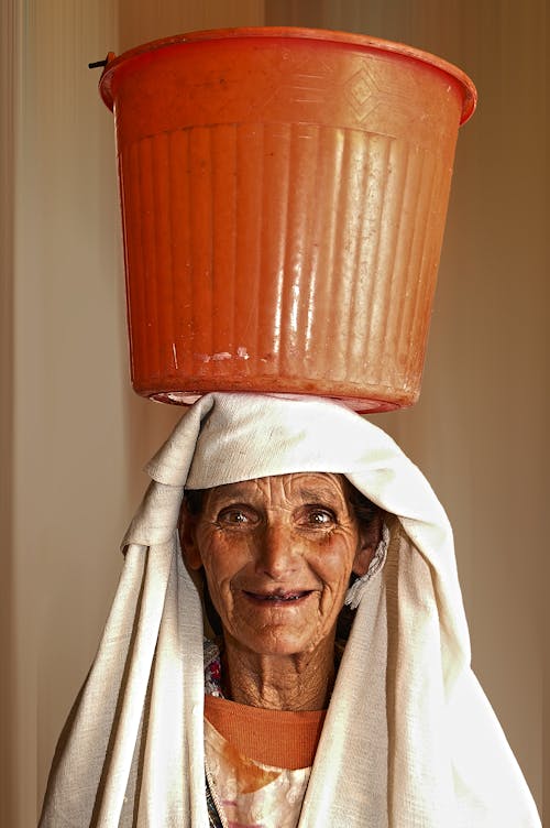 Портретное фото женщины с оранжевым пластиковым ведром на голове