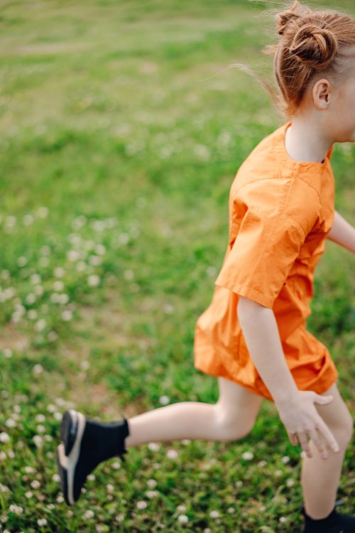 Free A girl in an orange dress running energetically through a grassy field, enjoying outdoor playtime. Stock Photo