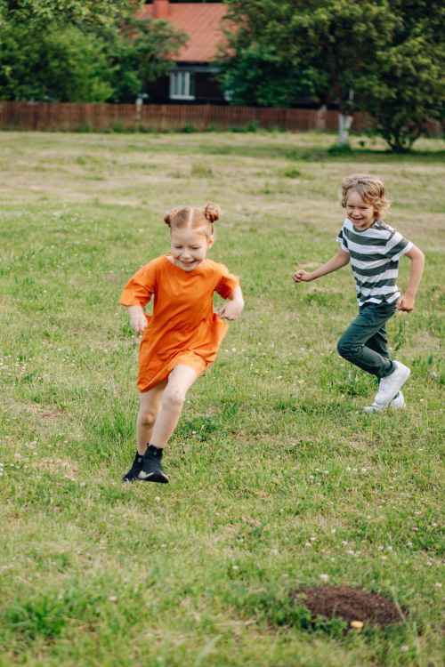 Free Two children playfully running on a sunny day in a lush green park. Stock Photo