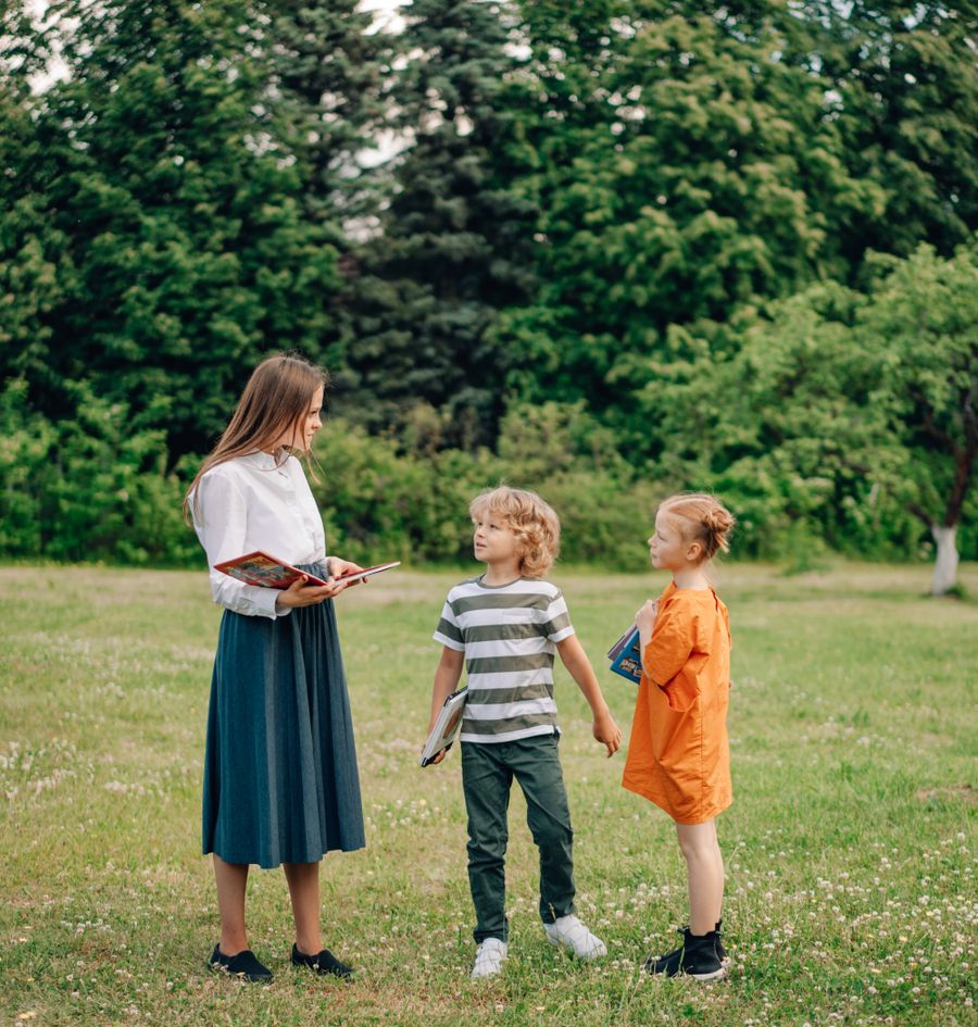 A teacher standing in a field talking with two children