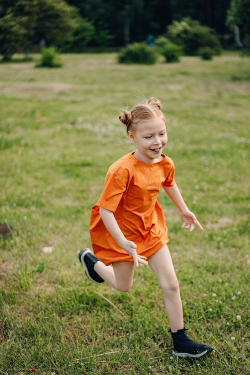 A Young Girl in Orange Dress Running at the Park