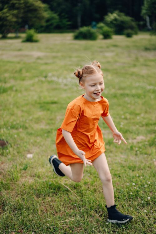 Free A happy young girl in an orange dress running playfully in a green park. Stock Photo