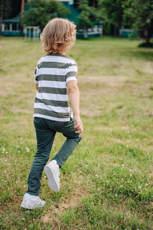 A Boy in Green and White Strip Shirt and Green Pants Walking on Grass Field