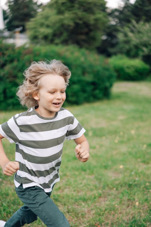 Free Blonde boy joyfully running in a lush green garden, enjoying outdoor play. Stock Photo