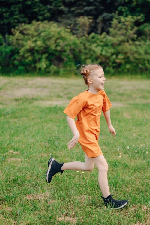 Free A happy child running in a green field wearing an orange dress, showcasing joy and freedom. Stock Photo
