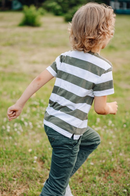 A Child in Black and White Striped Shirt Running on Grass
