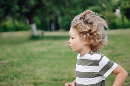 Free A Side View of a Young Boy in Striped Shirt Running at the Park Stock Photo