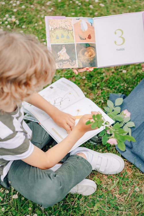 A Boy Sitting On Grass Reading A Book