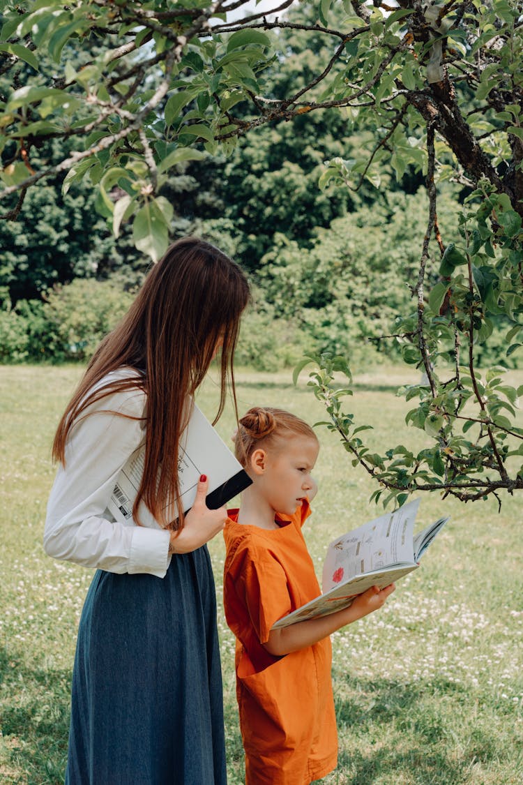 A Woman And A Child Holding Books Under A Leafy Tree